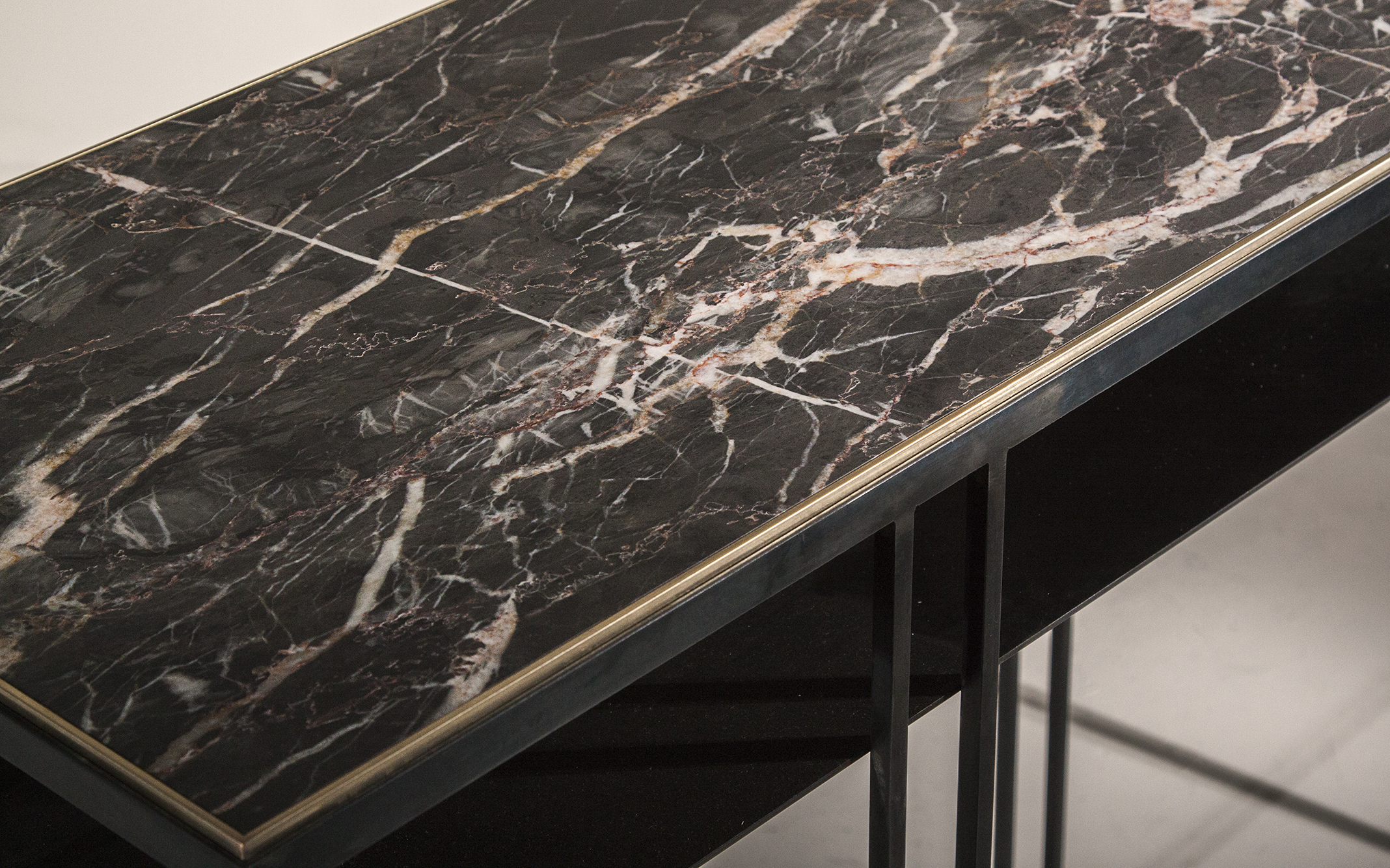 A console table in blackened steel and honed Moorcroft marble, with a polished brass trim.